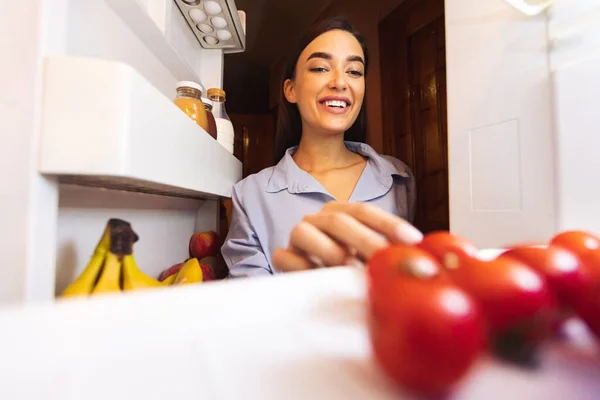 Jovem tomando tomate fresco da geladeira — Fotografia de Stock