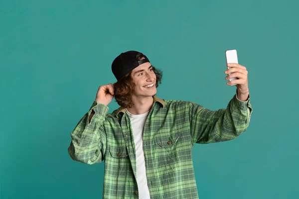 Neşeli genç hipster turkuaz arka planda akıllı telefonuyla selfie çekiyor. — Stok fotoğraf