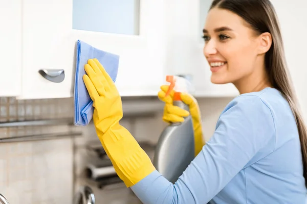 Muchacha de limpieza de muebles de cocina con trapo y spray —  Fotos de Stock