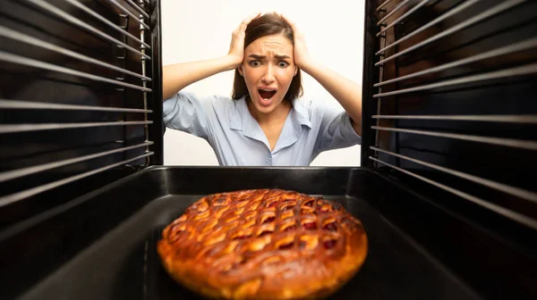 Šokovaná hospodyňka si prohlíží troubu, dívá se na spálený koláč — Stock fotografie