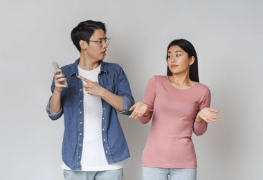 Asyalı adam kız arkadaşının cep telefonunu kontrol ediyor.