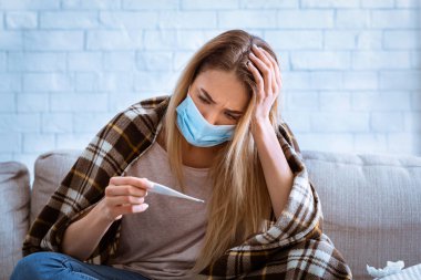 Kadın termometreye bakıyor. Kafaya tutunur.