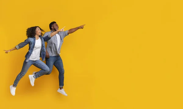 Positive black couple jumping in air and pointing at copy space — Stock Photo, Image