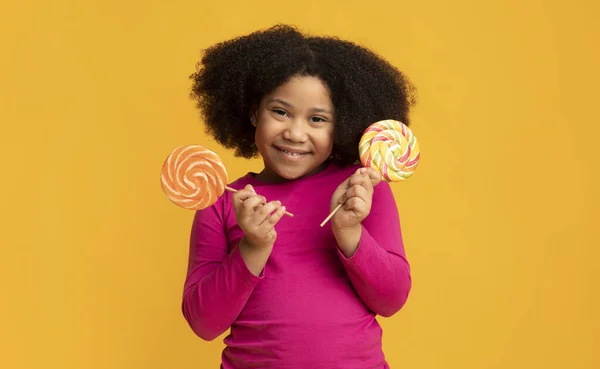 Mooi zwart meisje poseren met twee kleurrijke lolly 's in handen — Stockfoto