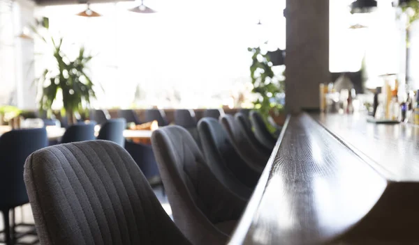 Langer verschwommener Tisch mit Stühlen in der Nähe der Bar mit Alkoholgetränken — Stockfoto