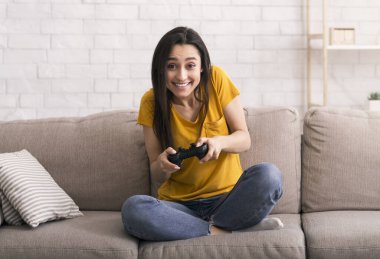 Karantina eğlenceleri. joystick 'li neşeli Latin kız evdeki kanepede video oyunları oynuyor.