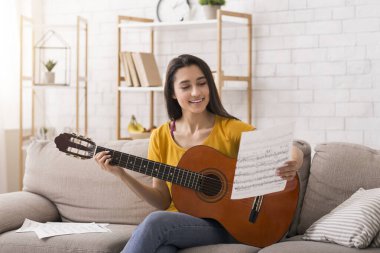 Eğlenceli ev aktiviteleri. Müzik sayfası ve gitarı olan güzel bir kız. Kanepede oturuyor.
