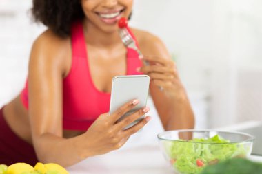 Akıllı telefon kullanan ve salata yiyen siyah bir kız.