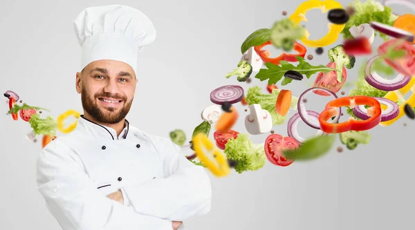 Egészséges receptek. Boldog szakács visel fehér egyenruha és zöldségek a levegőben szürke alapon. Kollázs — Stock Fotó