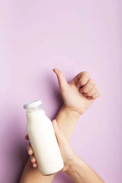 Скляна пляшка з кокосовим детоксикаційним напоєм у жіночій руці над фіолетовим — стокове фото