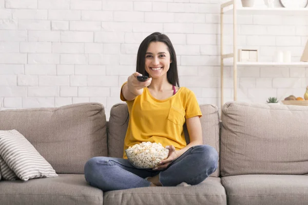 Blijf thuis vermaak. Mooi meisje met popcorn kijken TV op de bank in de woonkamer — Stockfoto