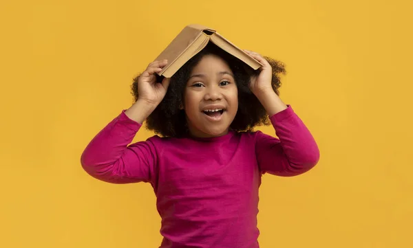 Pozytywny czarny dziewczynka dzierżąc otwartą książkę na głowie — Zdjęcie stockowe