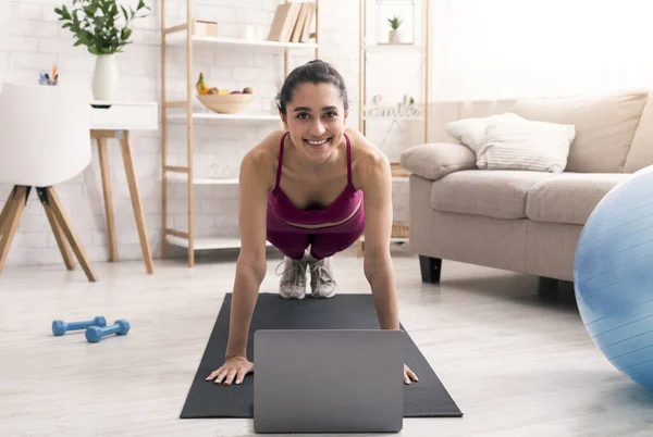 ऑनलाइन खेल ट्यूटोरियल। खुश लैटिन लड़की घर पर लैपटॉप के पास प्लैंक व्यायाम कर रही है — स्टॉक फ़ोटो, इमेज
