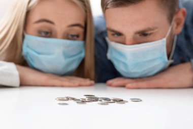 Koruyucu maskeli üzgün çift evde bozuk para yığınına bakıyor.
