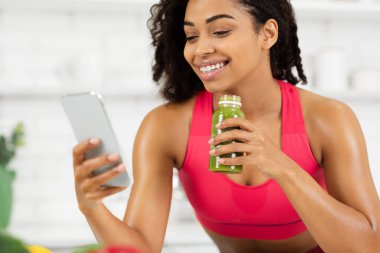 Siyah kız smoothie içiyor ve telefonunu kullanıyor.