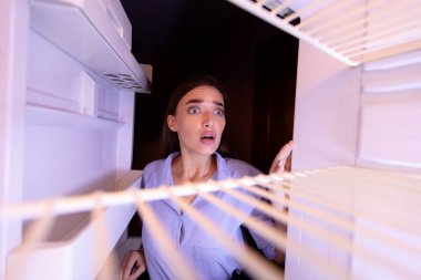 Çaresiz kız evde boş buzdolabını kontrol ediyor.