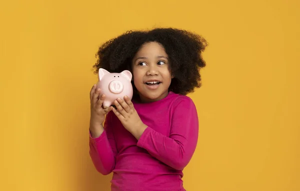 Retrato de adorable niña negra con su alcancía, fondo amarillo — Foto de Stock