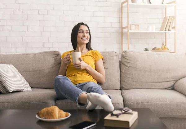 Manhã preguiçosa em casa. Menina alegre com xícara de bebida quente relaxante no sofá dentro de casa, espaço de cópia — Fotografia de Stock
