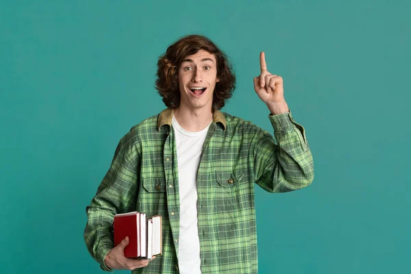 Opgewonden jonge student met boeken en notebook met briljant idee over kleur achtergrond — Stockfoto