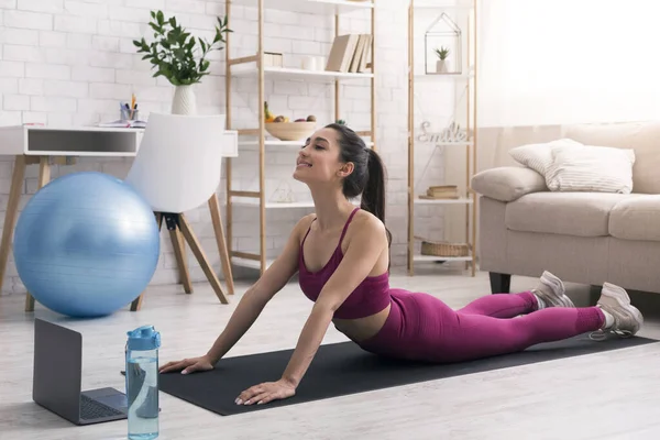 Stay at home fitness. Young girl doing back bend or snake yoga pose near laptop indoors