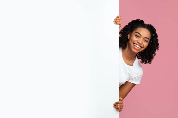 Fröhliche Afroamerikanerin blickt hinter leere Werbetafel — Stockfoto