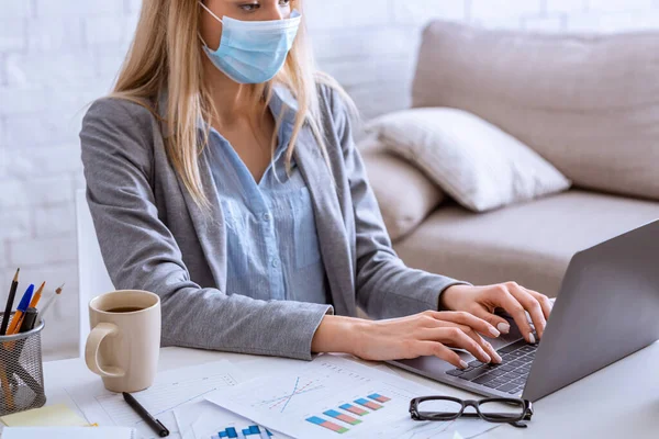 Bekerja selama coronavirus. Wanita bertopeng dengan laptop — Stok Foto