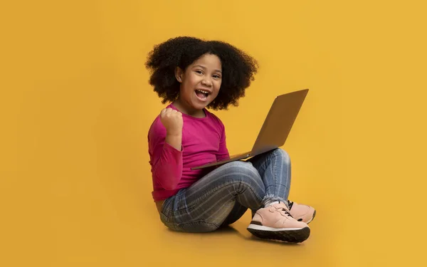Alegre niña afroamericana sentada con el ordenador portátil y celebrando el éxito — Foto de Stock