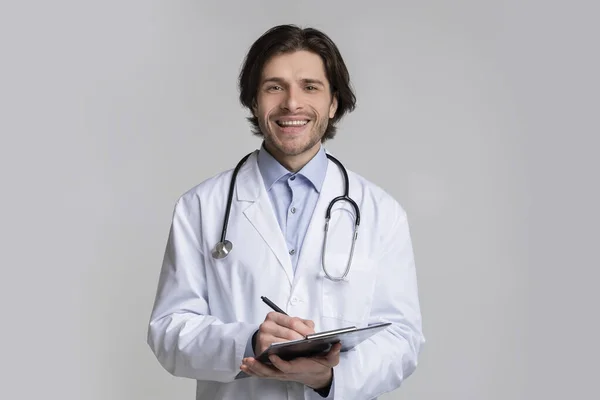 Retrato de médico masculino sorridente segurando prancheta e levando a história dos pacientes — Fotografia de Stock