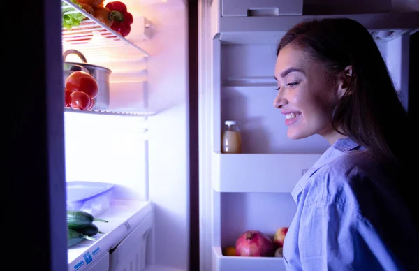 Χαρούμενο κορίτσι που ψάχνει για φαγητό στο ψυγείο αργά το βράδυ. — Φωτογραφία Αρχείου