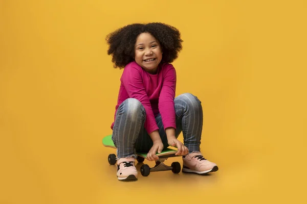 Ritratto di allegra ragazza nera seduta su skateboard moderno e ridente — Foto Stock