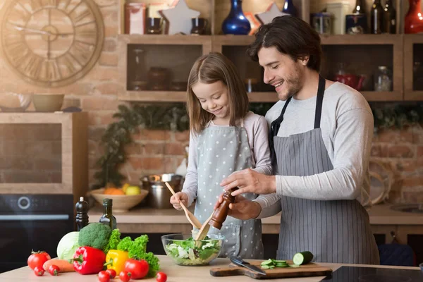 Junger Vater und Tochter kochen gemeinsam Mahlzeit und würzen Salat — Stockfoto