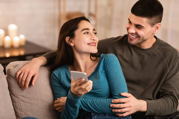 Пара с помощью мобильного телефона сидит на диване — стоковое фото