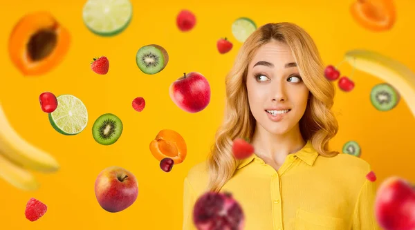 Menina loira bonita mordendo seu lábio e frutas no ar, colagem com espaço de cópia — Fotografia de Stock
