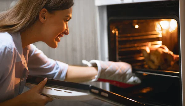 Mulher feliz tomando frango assado do forno em casa — Fotografia de Stock