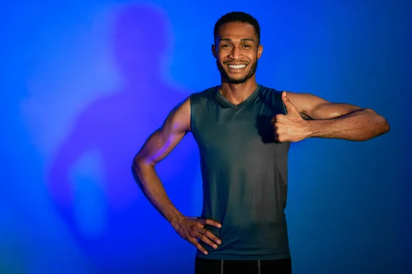 Fit Man Gesturing Duimen omhoog glimlachend staande over blauwe achtergrond — Stockfoto