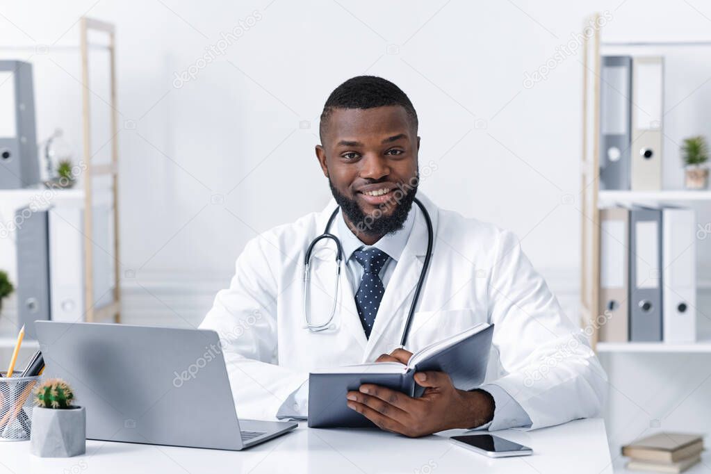 Busy black doc working with laptop in his office