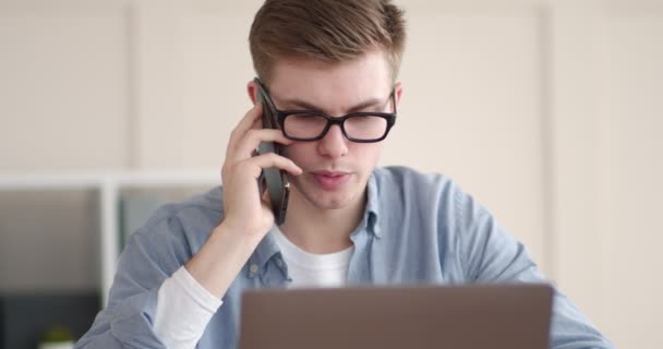 Serieuze man praten over de telefoon en werken op de laptop — Stockvideo