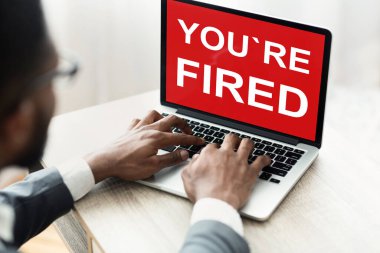 Endişeli Afrikalı Amerikalı bir adam. Üzerinde yazı olan dizüstü bilgisayara bakıyor. Kovuldun.