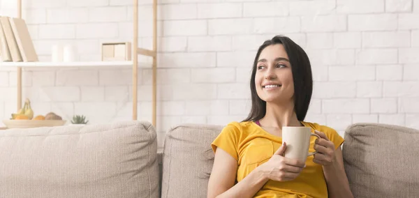 Vreedzaam weekend thuis. Millennial meisje genieten van haar koffie op de bank binnen, lege ruimte. Panorama — Stockfoto