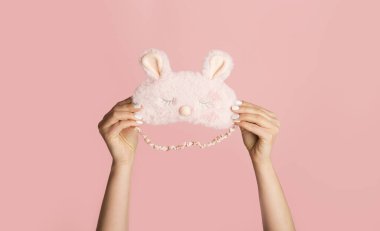 Tanımlanamayan milenyum kızı pembe arka planda sevimli bir tavşan uyku maskesi tutuyor.