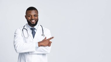 Kolları çaprazlanmış dost canlısı siyah doktor boş uzayı işaret ediyor.