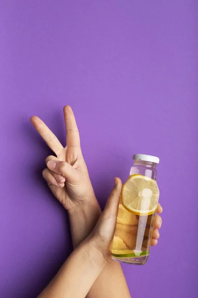 Женщина держит бутылку с детоксикационным лимонадом и показывает V знак — стоковое фото