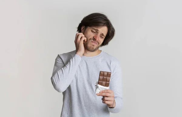 Homem coça a bochecha e olha para o chocolate — Fotografia de Stock