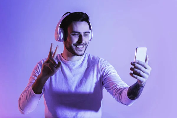 Sorrindo cara mostrando sinal de paz no smartphone — Fotografia de Stock