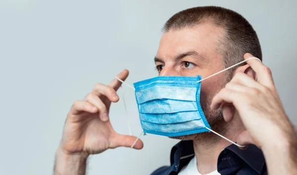 Homem que põe na máscara para a prevenção do coronavírus sobre o fundo cinzento — Fotografia de Stock