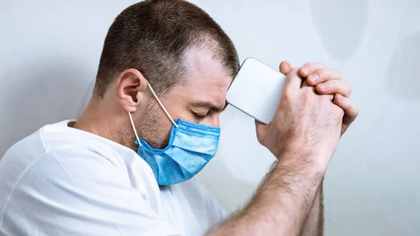 Depressed Man In Protective Mask Holding Cellphone Sitting Indoor Alone