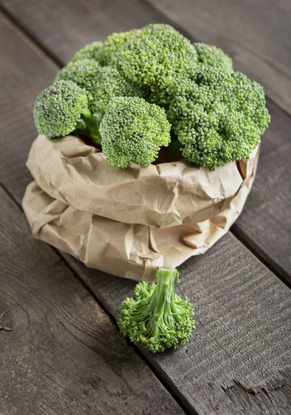 Świeże brokuły w papierowej torbie na drewnianym tle — Zdjęcie stockowe