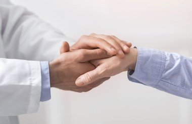 Doktor, tıbbi muayenede yaşlı kadının elini tutuyor.