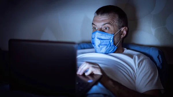 Homem lendo notícias no laptop deitado na cama à noite — Fotografia de Stock