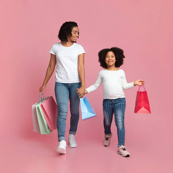 Vrolijke Afrikaanse moeder en dochter wandelen met boodschappentassen en glimlachen — Stockfoto